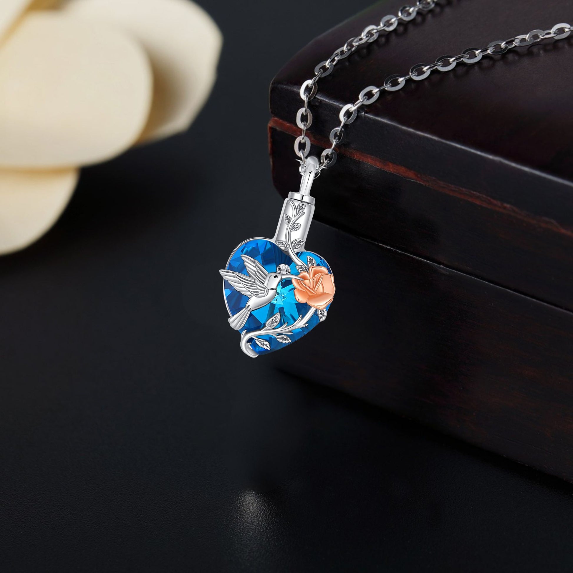 Decorative necklace with a blue pendant featuring a bird and flower design on a dark background.