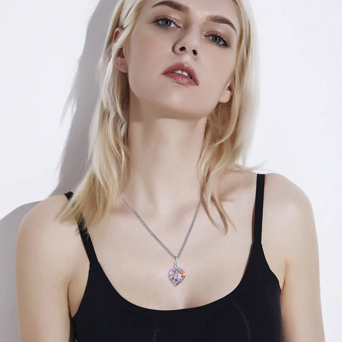 Heart-shaped pendant with a hummingbird, rose, and purple gemstone on a white background