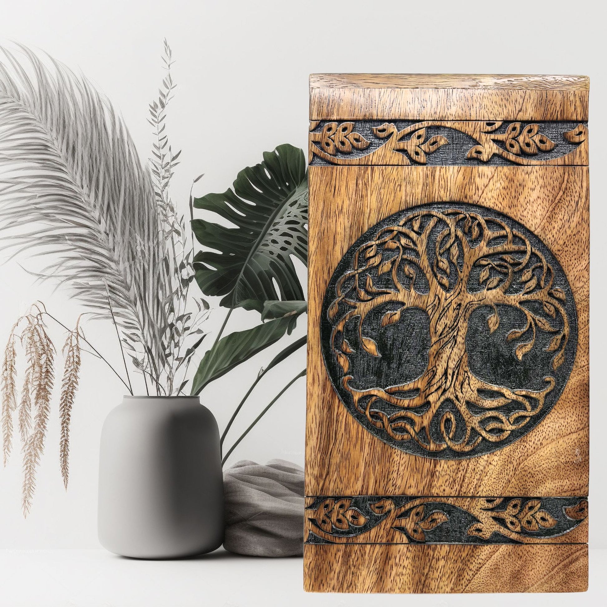 Wooden box with tree of life design against a white background with plants.