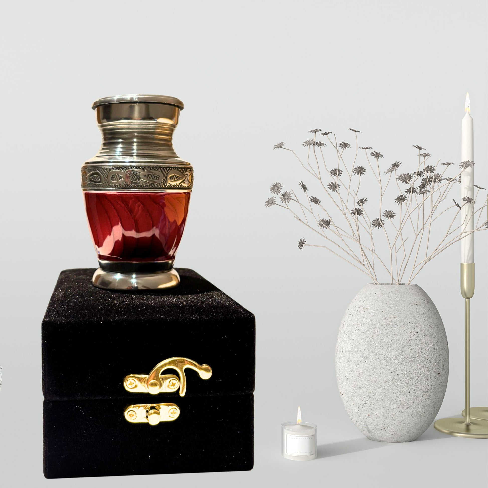 Red glass urn on a black base with decorative elements, next to a white vase and candle.