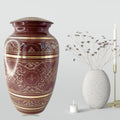 Decorative urn with intricate patterns next to a smaller vase and candle on a light gray background