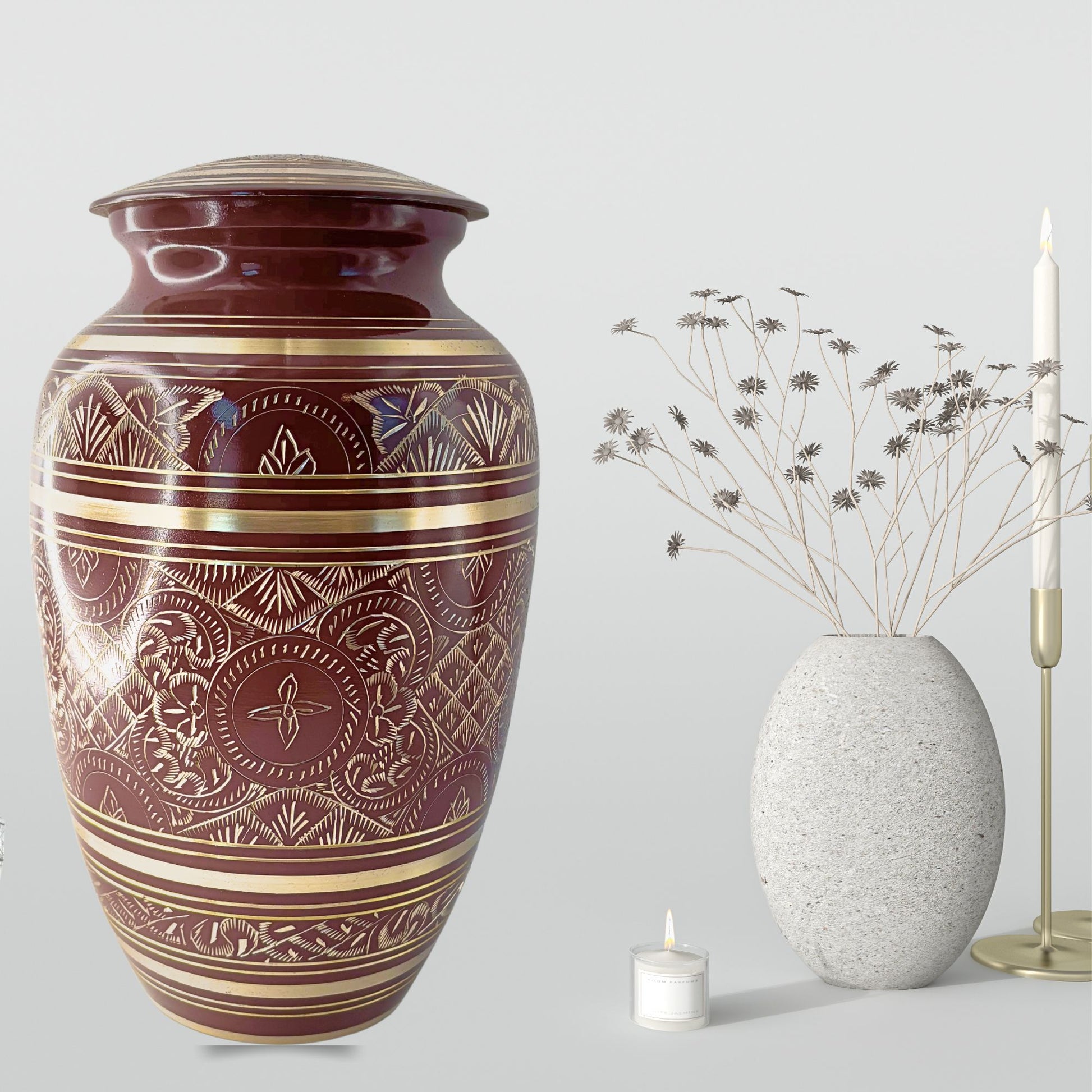 Decorative urn with intricate patterns next to a smaller vase and candle on a light gray background