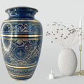 Blue decorative urn with gold patterns next to a smaller white vase and candle on a light gray background