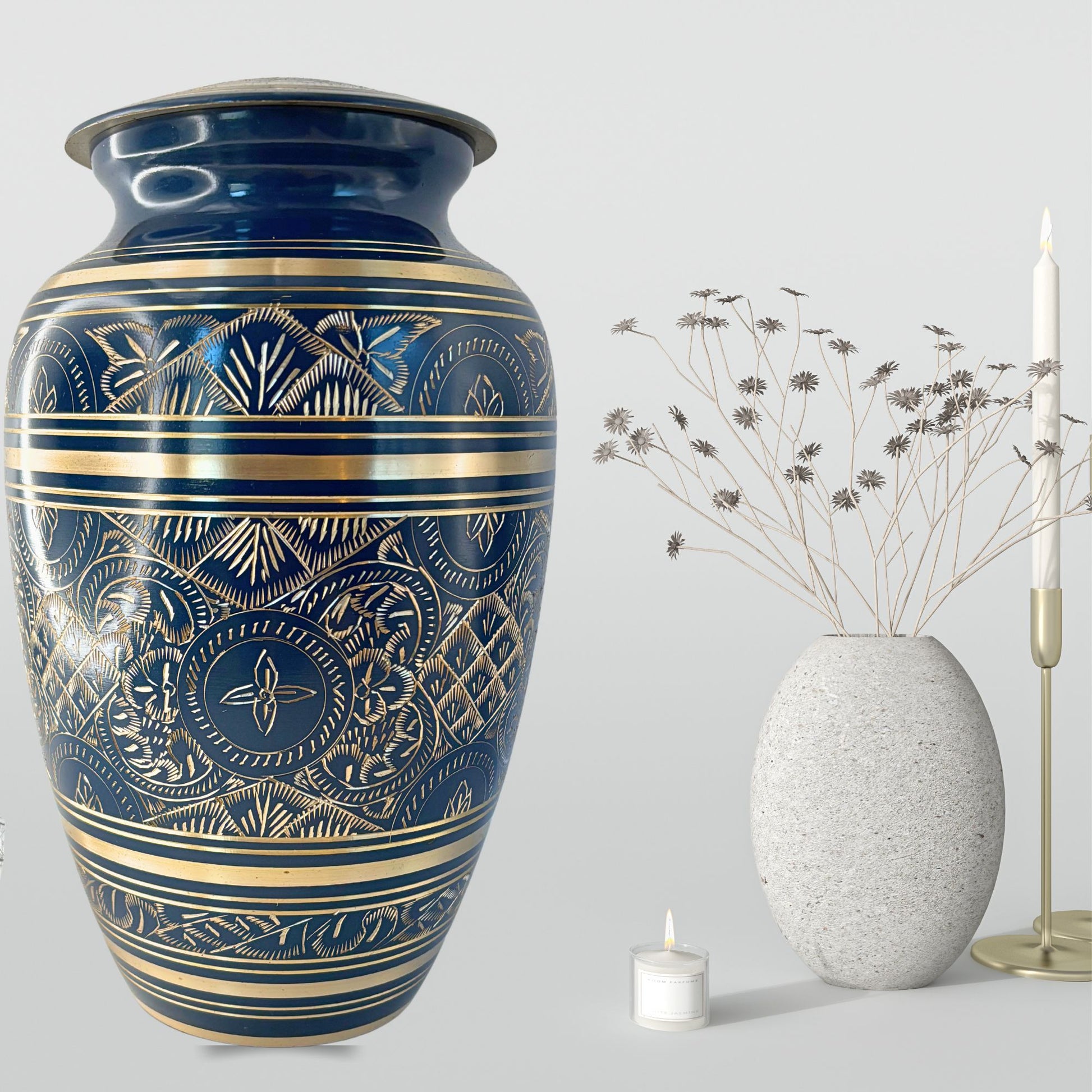 Blue decorative urn with gold patterns next to a smaller white vase and candle on a light gray background