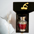 Red and silver urn in a black box with gold accents on a white background