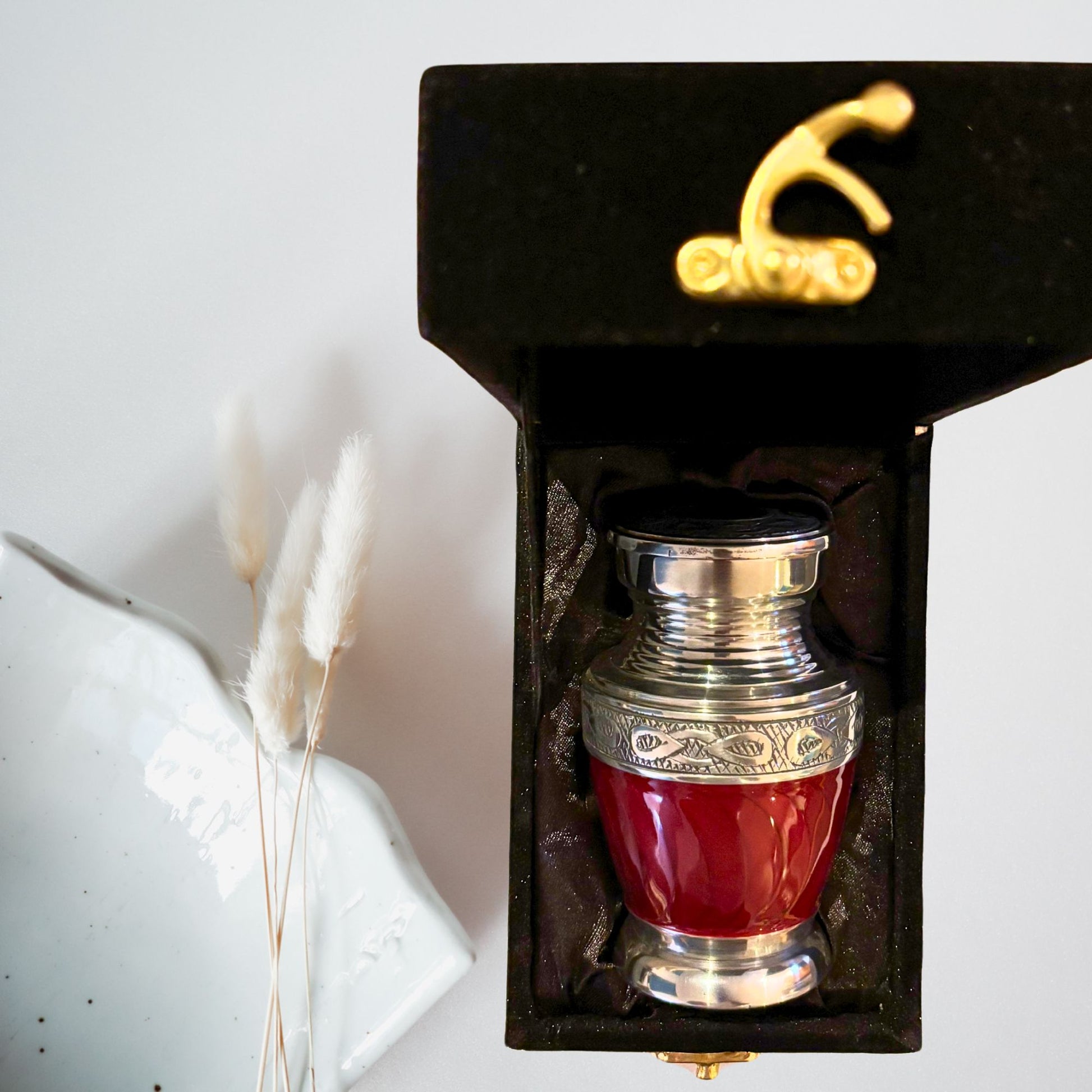 Red and silver urn in a black box with gold accents on a white background