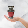 Silver urn with red liquid held in a hand against a white background