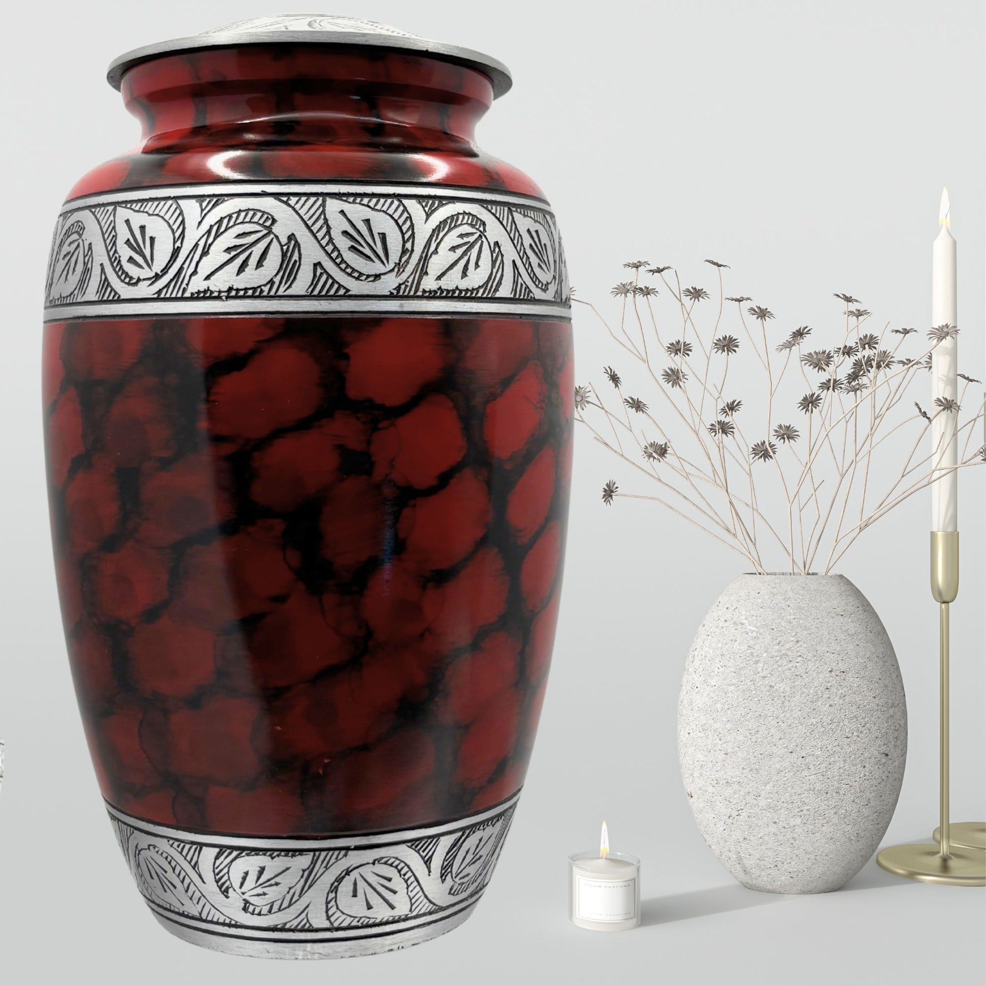 Red and black patterned urn with a white candle and decorative vase on a light gray background