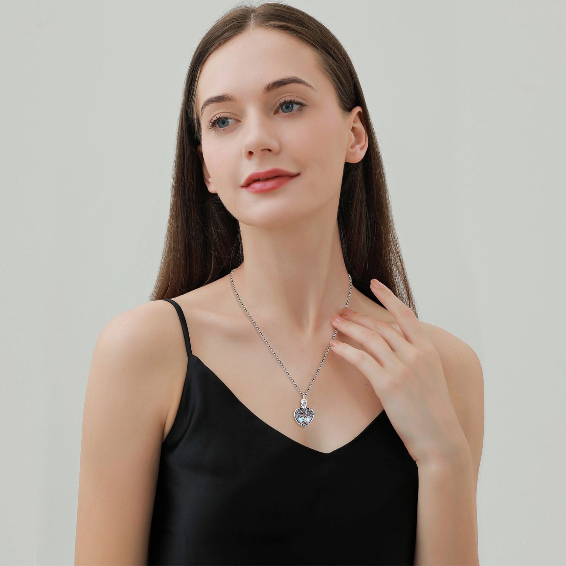 Woman wearing a necklace with a heart pendant against a plain background