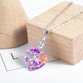 Necklace with a purple heart-shaped pendant featuring a bird and rose design on a wooden block.