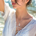 Woman wearing a silver necklace with a heart pendant by a body of water.