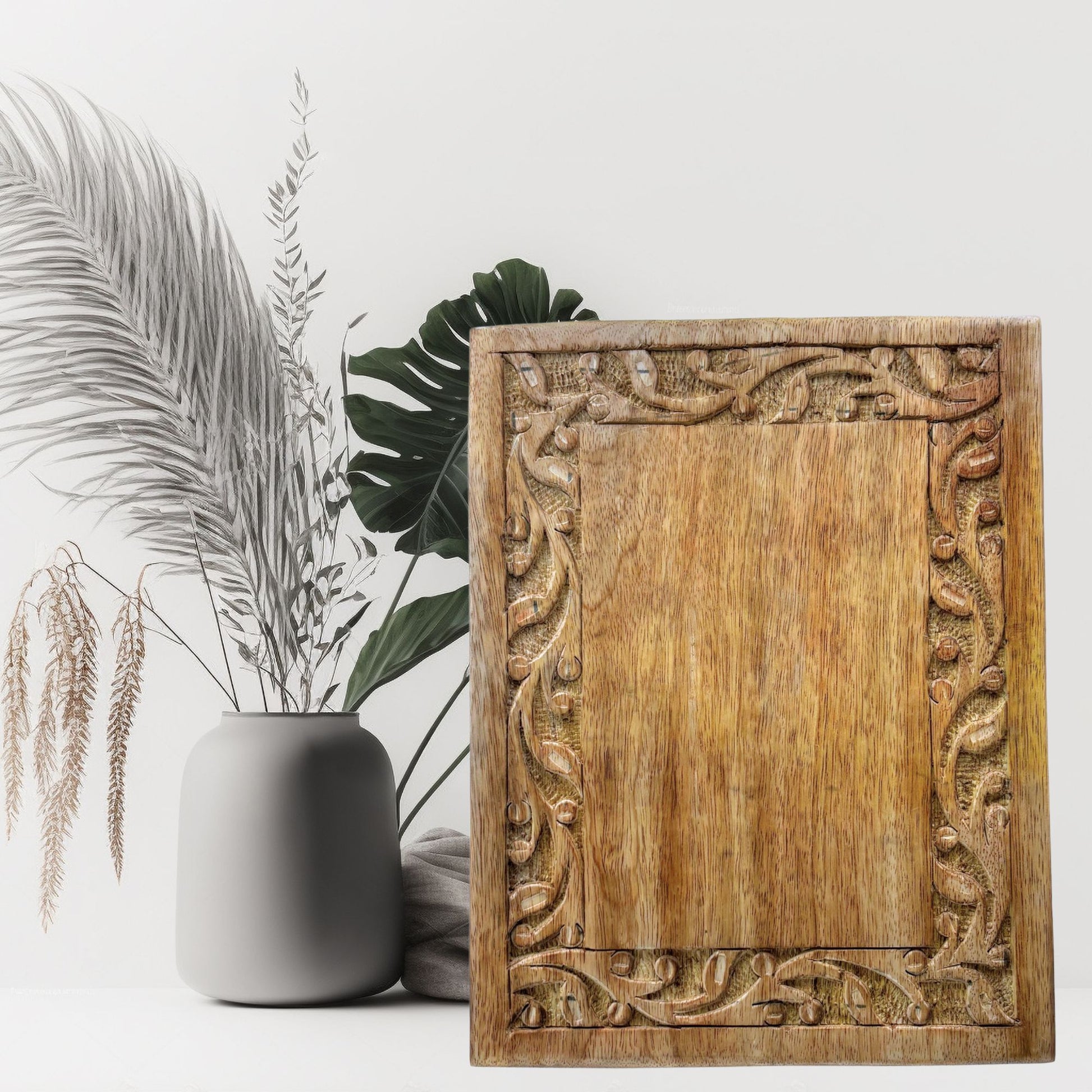 Wooden decorative panel with intricate carvings next to a vase and plants on a white background