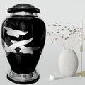 Black urn with silver fish designs on a gray background