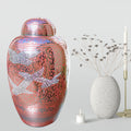 Decorative urn with bird design next to a white candle and textured vase on a light gray background