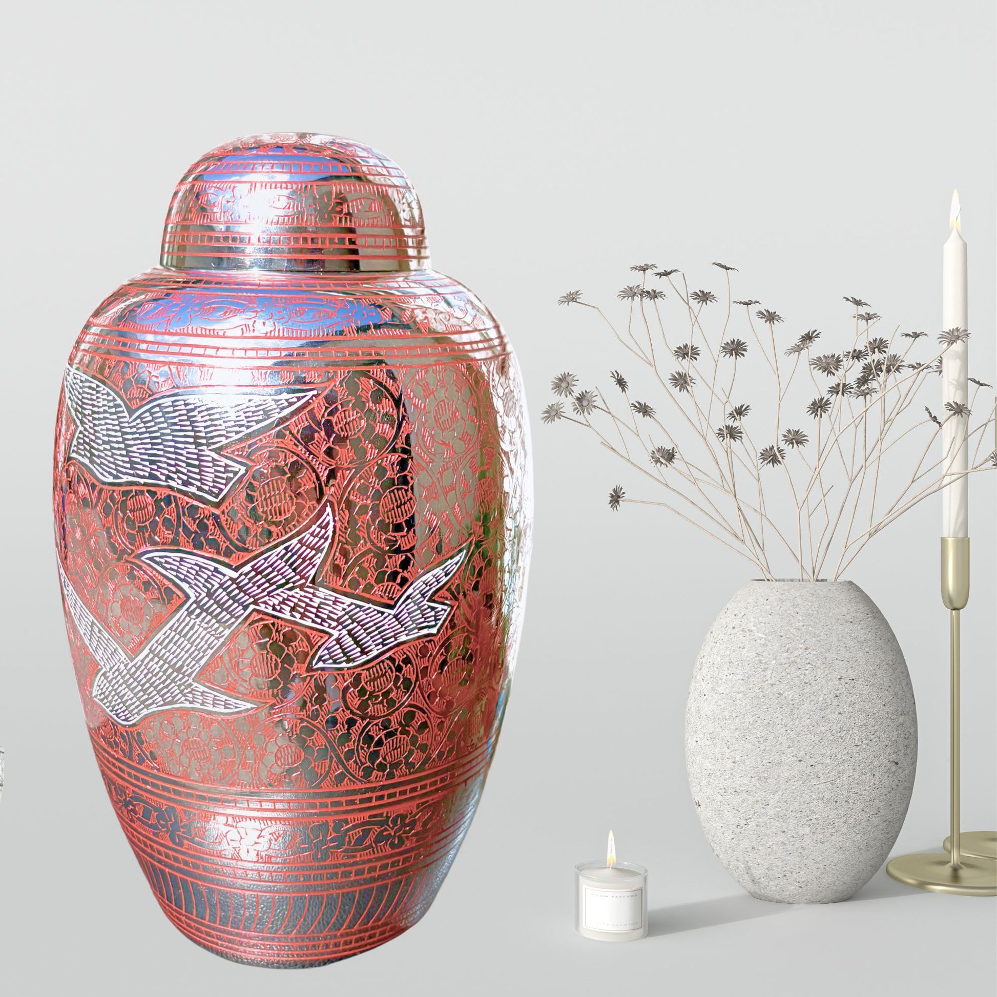 Decorative urn with bird design next to a white candle and textured vase on a light gray background