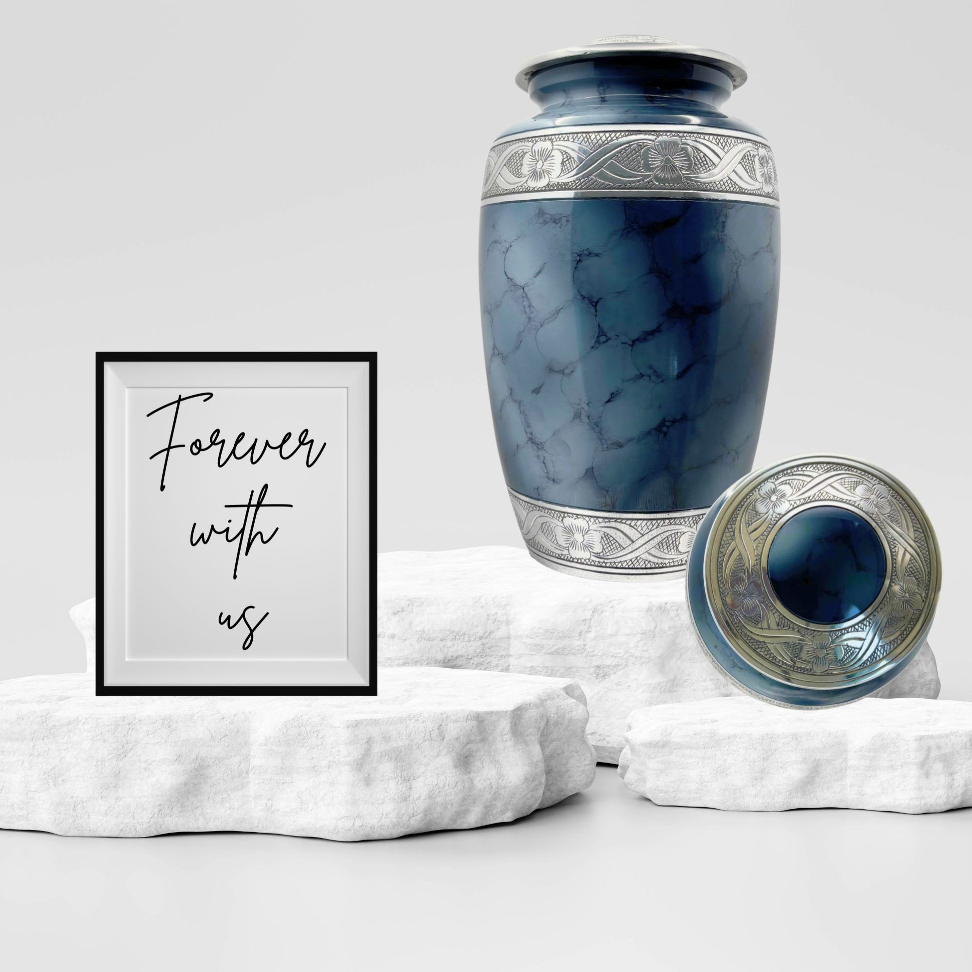Blue urn with silver detailing on a white marble surface, accompanied by a framed quote 'Forever with us'.